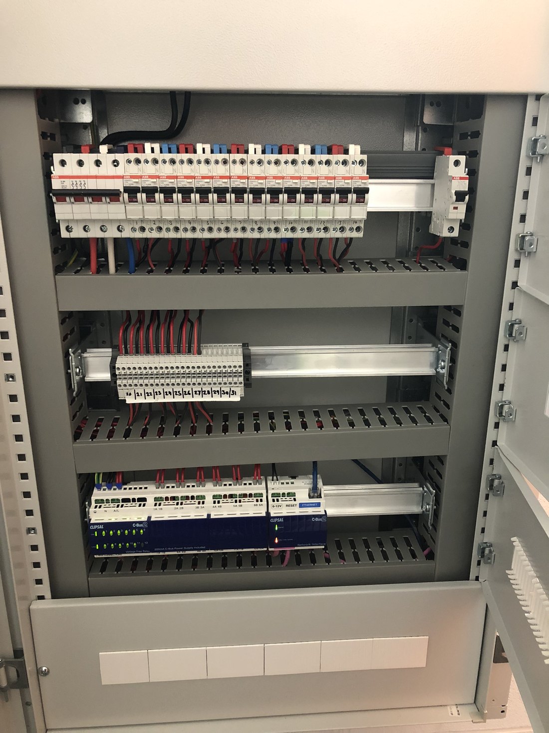 An open switchboard with a row of labelled breakers, numbered terminals and Clipsal C-Bus modules