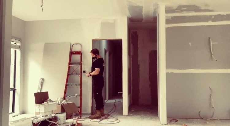An electrician fitting a wall switch in a house mid-renovation, plasterboard freshly stopped