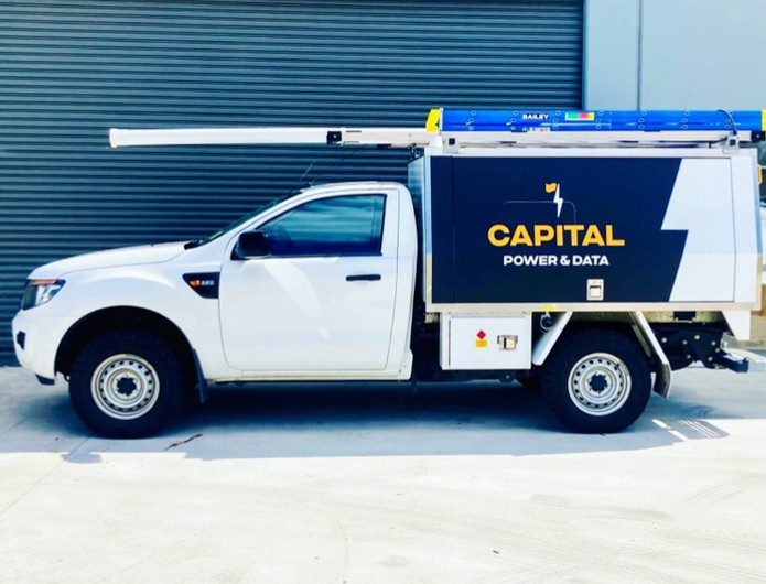 The white Capital Power & Data work ute with its navy and orange branded canopy and ladders on the rack